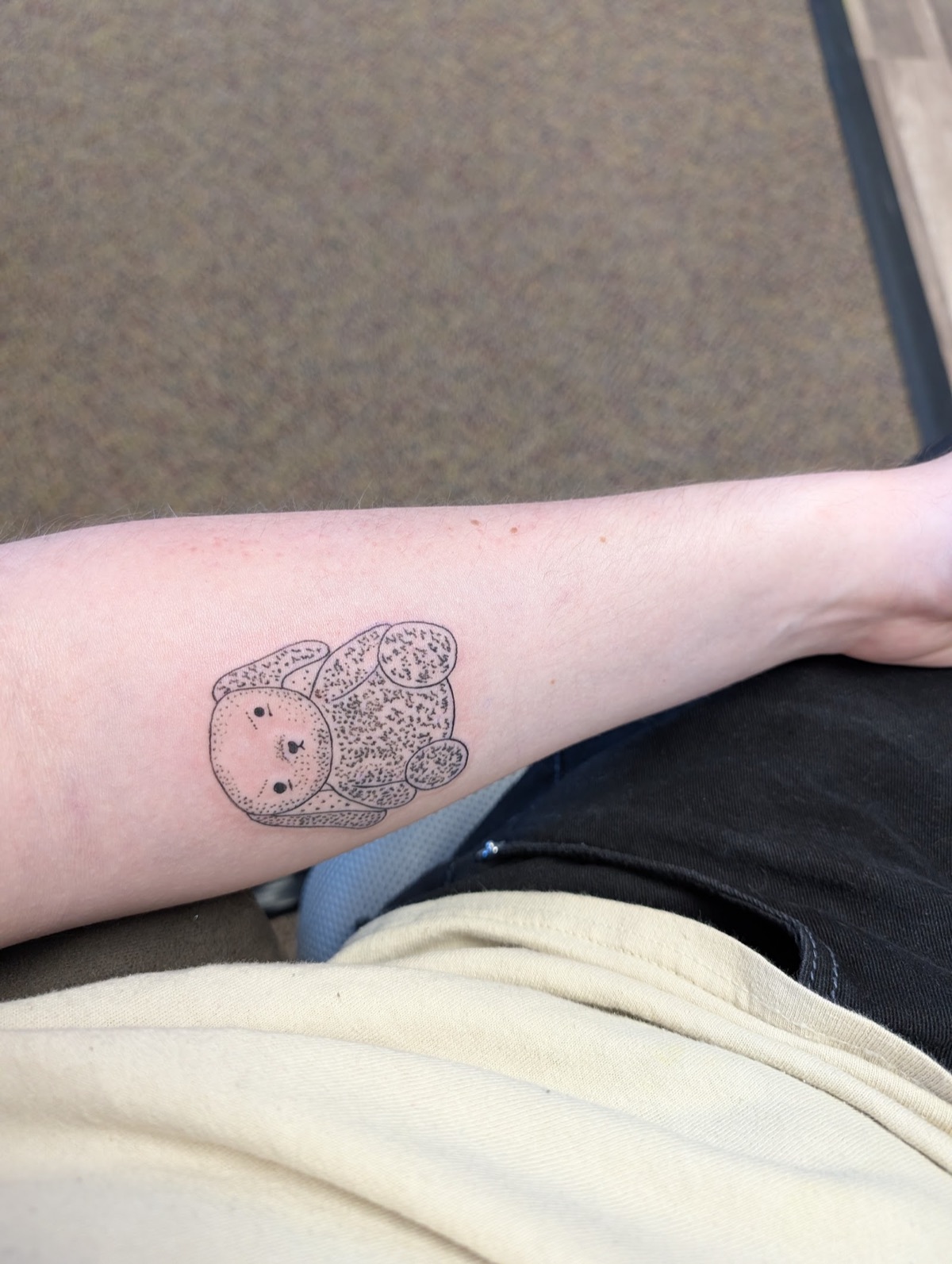 Small fine-line plush bear tattoo on an inner forearm, taken from a client's sketch.