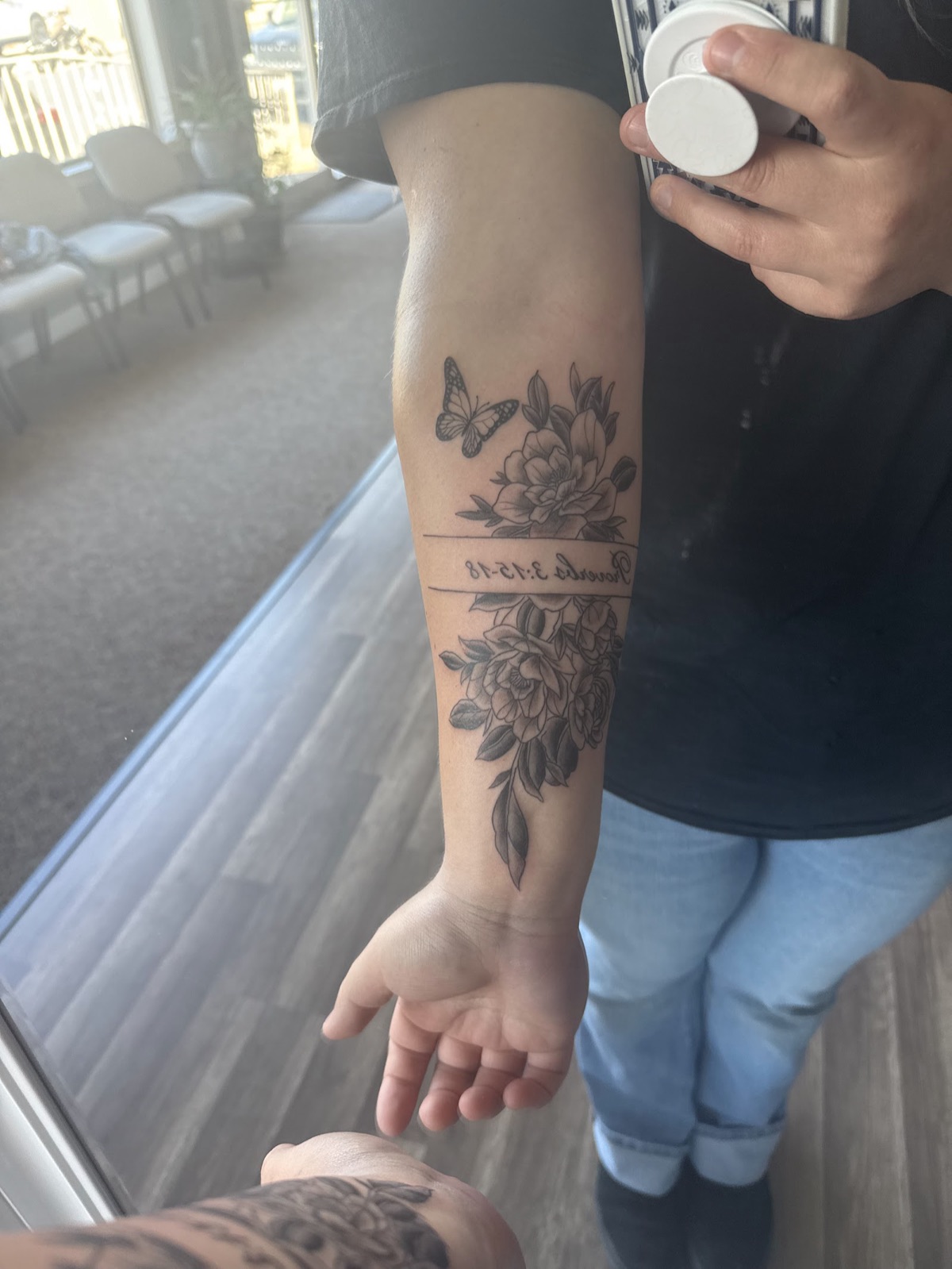 Floral forearm tattoo with peonies, a butterfly and a date in script.
