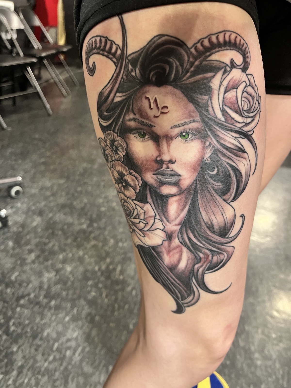 Black and grey portrait tattoo of a woman with ram horns and roses on a thigh.